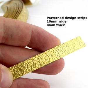 May include: A gold-coloured patterned design strip, 10mm wide and 8mm thick, held between fingers. The strip has a textured surface with a repeating pattern. The text in the image reads: "Patterned design strips 10mm wide 8mm thick."