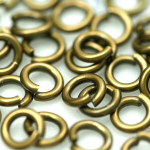 May include: A close-up of a pile of small, gold-colored jump rings. The rings are all the same size and are made of metal.