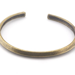 Op de afbeelding: Een eenvoudige, goudkleurige metalen armband. De armband is glad en heeft een licht afgeronde vorm.