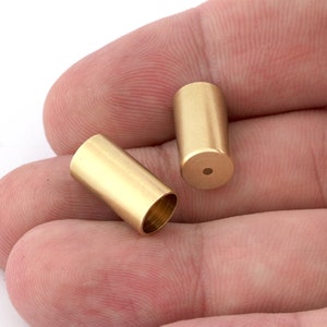 May include: Two gold-colored metal caps with a smooth, cylindrical shape. The caps are hollow and have a small hole at the bottom.