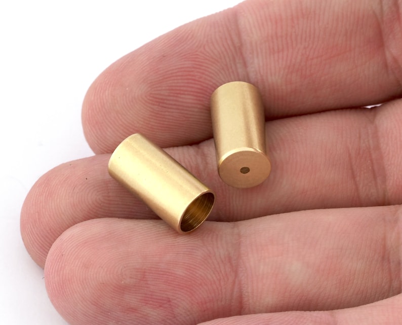 May include: Two gold-colored metal caps with a smooth, cylindrical shape. The caps are hollow and have a small hole at the bottom.