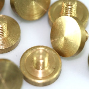May include: A close-up of a group of brass screw-on knobs. The knobs are round and have a smooth, polished finish. They are all the same size and shape.