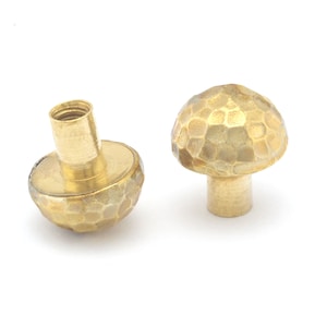 May include: Two gold-toned metal mushroom-shaped cabinet knobs with a hammered texture.
