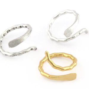 Könnte beinhalten: Zwei silberne und ein goldener Ring, die verdreht sind. Die Ringe sind aus Metall und haben eine strukturierte Oberfläche.