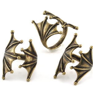 Puede incluir: Tres anillos de color dorado con un diseño de ala de murciélago. Los anillos son ajustables y tienen un estilo gótico único.