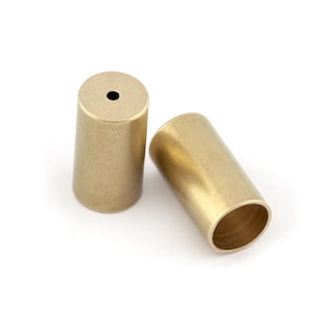 May include: Two gold-colored metal end caps for a cord or rope. The end caps are cylindrical and have a smooth, slightly textured surface.