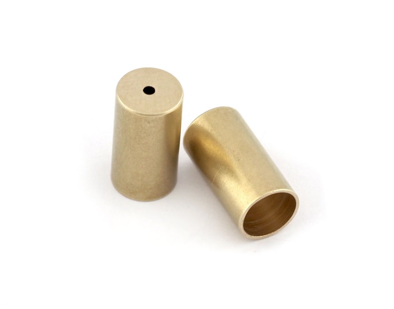 May include: Two gold-colored metal end caps for a cord or rope. The end caps are cylindrical and have a smooth, slightly textured surface.