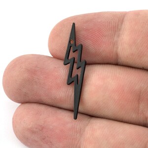 Op de afbeelding: Zwarte metalen bliksem-bedel met een gat aan de bovenkant om te bevestigen aan sieraden of andere knutselwerkjes.