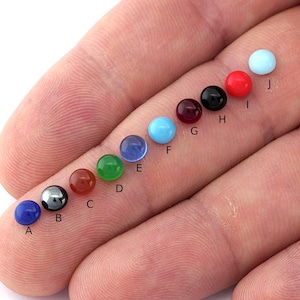 Puede incluir: Una fila de diez piedras preciosas redondas de varios colores, etiquetadas de la A a la J. Las piedras preciosas están dispuestas de izquierda a derecha en el siguiente orden: azul, gris, marrón rojizo, verde, azul, turquesa, rojo, negro, rojo y azul claro.