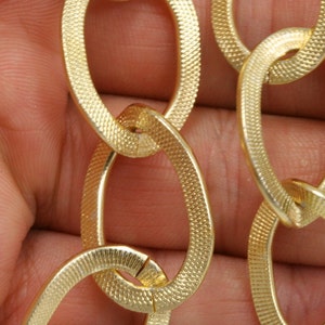 May include: Close-up of a gold chain with oval links. The chain has a textured surface.