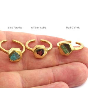 Könnte beinhalten: Drei goldfarbene Ringe mit sechseckigen Fassungen, jeweils mit einem anderen Edelstein: blauem Apatit, afrikanischem Rubin und Mali-Granat. Die Ringe sind offen, um die Größe anzupassen. Die Edelsteine sind sichtbar.