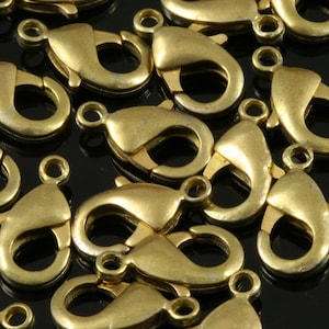 May include: A close-up of a group of gold-toned metal lobster claw clasps. The clasps are arranged in a random pattern on a black surface.