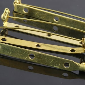 May include: Four gold-toned metal pin back closures. The closures are designed to be used for attaching brooches, pins, or other jewellery to fabric.