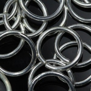May include: A close-up of a pile of silver jump rings. The rings are all the same size and are arranged in a random pattern.
