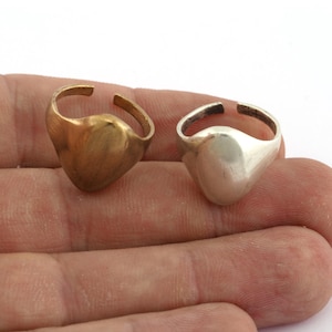 Könnte beinhalten: Zwei schlichte Ringe aus Silber und Gold mit abgerundeter, ovaler Oberseite. Die Ringe werden an einem Finger gezeigt.