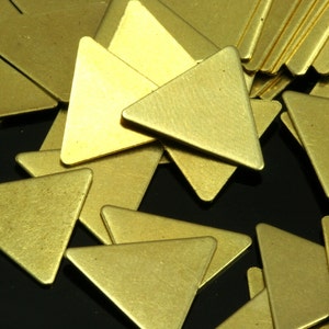 May include: A pile of gold-colored metal triangle shapes. The triangles are scattered on a black surface.