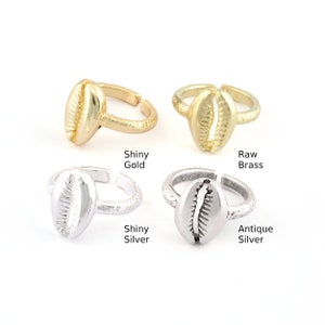May include: Four adjustable rings featuring a cowrie shell design. The rings are available in shiny gold, raw brass, shiny silver, and antique silver.