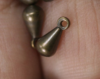May include: A close-up of a gold-toned metal pendant with a teardrop shape and a small loop at the top.