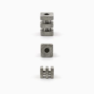 May include: Three metal components are displayed against a white background. One is a stack of three square blocks with a hole in the center. Another is a single square block with a hole. The third is a small rectangular piece with three vertical bars.