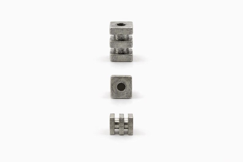 May include: Three metal components are displayed against a white background. One is a stack of three square blocks with a hole in the center. Another is a single square block with a hole. The third is a small rectangular piece with three vertical bars.