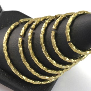 May include: A collection of gold-colored, hammered metal hoop earrings. The earrings are open at one end and have a textured, faceted surface. They are displayed on a black stand.