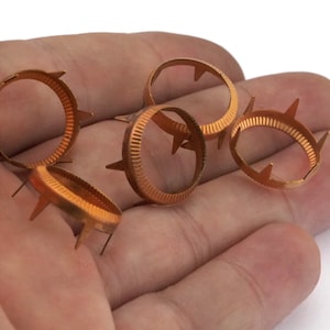 May include: Six copper-colored metal rings with pointed edges. The rings are designed to be used as a decorative embellishment for crafts.
