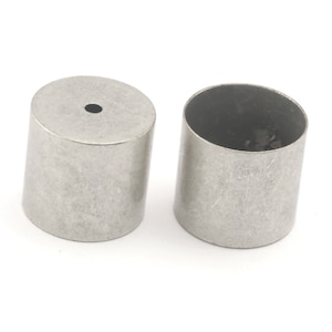 May include: Two small, cylindrical metal objects with a brushed finish. One has a small hole in the top. The objects are silver-coloured and appear to be made of stainless steel or a similar metal. They are set against a white background.