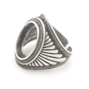 May include: Silver ring with a round bezel setting and a decorative design of stylized feathers. The ring is designed to hold a cabochon stone.