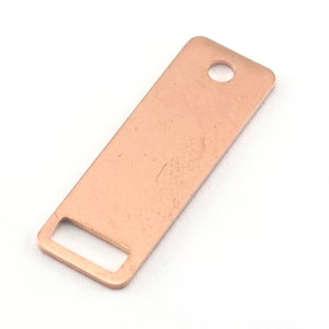 May include: A copper-colored rectangular metal tag with a rectangular cutout at one end and a circular hole at the other. The tag has a smooth, slightly textured surface and is set against a white background.