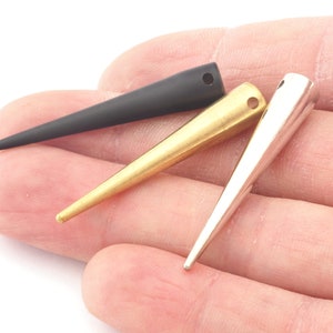 May include: Three pointy metal tips in black, gold, and silver. The tips are in the shape of a cone and have a small hole at the top.