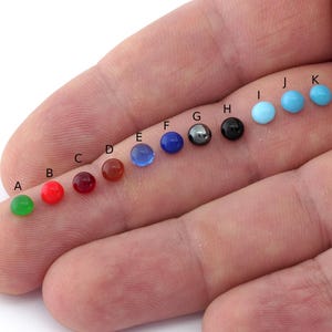 May include: A row of 11 round gemstones in various colours, including green, red, blue, black, and turquoise. The gemstones are labelled with letters A through K.