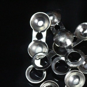 Op de afbeelding: Zilveren metalen oogjes met een ronde vorm en een verhoogd midden. De oogjes zijn verbonden door metalen ringen.
