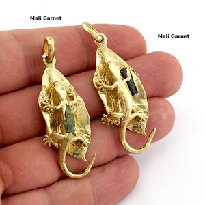 May include: Two gold-colored lizard pendants, each with a Mali Garnet stone. The lizards are attached to a leaf-shaped backing. The text "Mali Garnet" is printed above the pendants.