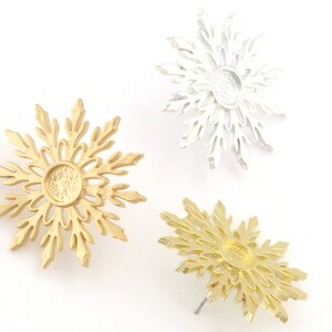 May include: Three snowflake-shaped metal charms, two gold and one silver, with a circular opening in the center. The charms are perfect for jewelry making or crafting.