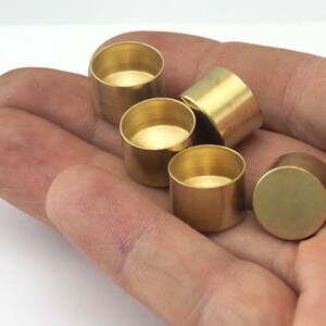 May include: A collection of small, cylindrical brass components. The objects are golden in color and have a smooth, reflective surface. The components are held in a hand, showcasing their size and shape. They appear to be small containers or decorative elements.