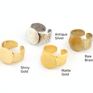 Könnte beinhalten: Vier verstellbare Ringe in verschiedenen Ausführungen: Antik-Silber, glänzendes Gold, mattes Gold und rohes Messing. Jeder Ring hat eine runde, flache Oberfläche.