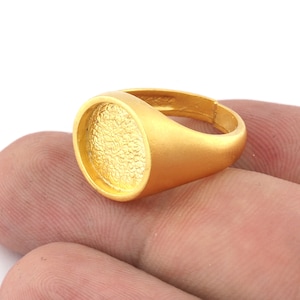 May include: A gold ring with a round, textured top. The ring is made of metal and has a smooth, polished finish.