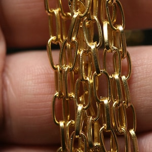 May include: A close-up of a gold chain made of multiple strands of linked oval-shaped links.
