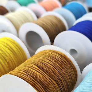 May include: Close-up of spools of colorful thread wound around white plastic bobbins. The threads are various colors, including yellow, blue, brown, and green.
