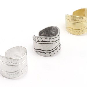 Op de afbeelding: Drie verstelbare oor manchet in zilver- en goudtinten. De manchetten hebben geëtste ontwerpen, waaronder golvende lijnen en gestippelde patronen. De sieraden worden gepresenteerd tegen een witte achtergrond, waarbij de metalen afwerkingen en ingewikkelde details worden benadrukt.