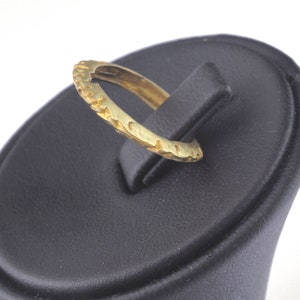 May include: A gold ring with a textured band. The ring is displayed on a black ring display stand.