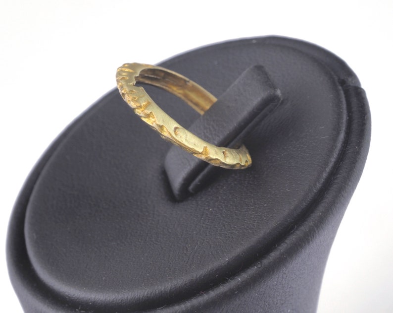 May include: A gold ring with a textured band. The ring is displayed on a black ring display stand.