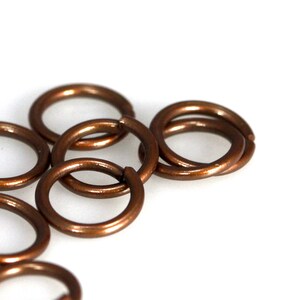 May include: A close-up of several small, copper-coloured jump rings. The rings are interlocked, creating a chain-like pattern.