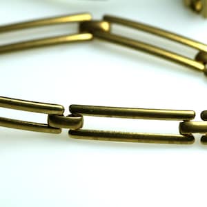 Puede incluir: Un brazalete de metal dorado con un diseño de cadena de doble eslabón.