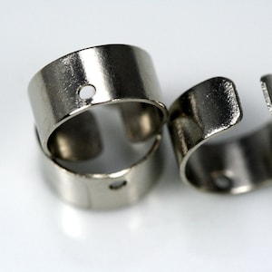 May include: Three silver metal rings with a small hole in each. The rings are stacked on top of each other.