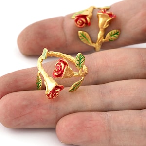 May include: Two gold rings featuring red roses and green leaves. The rings are designed to resemble a rose stem with leaves and flowers.