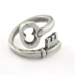 Puede incluir: Un anillo de plata en forma de llave con un agujero en forma de corazón en la llave. El anillo está abierto y se puede ajustar para que se ajuste a diferentes tamaños de dedos.