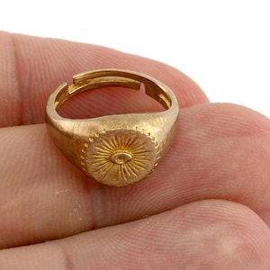 Può includere: Un anello regolabile color oro con un design a raggiera sulla parte superiore. La parte superiore dell'anello ha una forma ovale centrale all'interno del motivo a raggiera. L'anello è in metallo con finitura opaca.