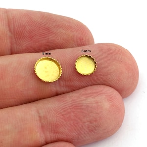 Puede incluir: Se muestran dos pequeñas bandejas de bisel doradas, una de 8 mm y otra de 6 mm de diámetro. Las bandejas tienen un borde festoneado y una superficie interior plana. Estos componentes probablemente se utilizan para la fabricación de joyas o manualidades.