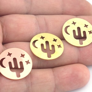 May include: Three gold-colored metal charms with a cactus, moon, and stars design. Each charm is round and has a cut-out design.